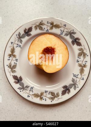 Halbe Nektarine auf dem Royal Doulton Burgundy-Schild. Fertig zum Essen. Stockfoto