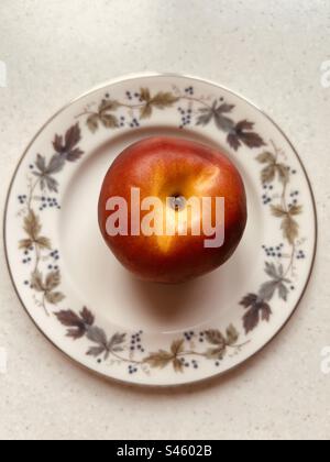 Nektarine auf einem königlichen Doulton Burgundy-Teller. Fertig zum Essen. Stockfoto