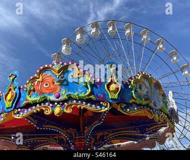 Die dekorativen Farben und Formen auf der Spitze des Kinderkreislaufs kontrastieren mit dem schlichten Weiß des Big Wheel in Bangor, Nordirland. In der Nähe des Jachthafens gibt es zahlreiche Aktivitäten für Kinder. Stockfoto