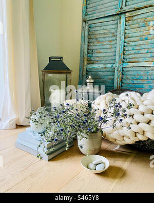 Fotos aus dem Stilleben von Büchern, zarten violetten Blumen in einem Topf, Steinen in einer Schüssel, Wolldecke, Kerzen und venezianischen Holzjalousien. Stockfoto