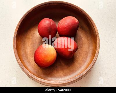 Vier Nektarinen in einer runden Holzschüssel. Kopfschuss. Stillleben. Frisch, bunt, saftig, süß, nahrhaft, Sommerfrucht. Stockfoto