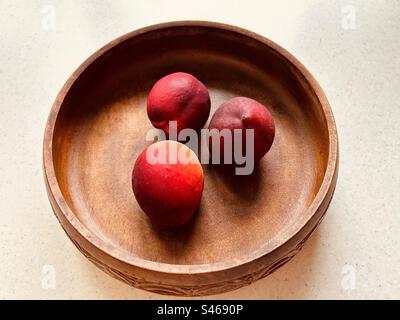 Drei Nektarinen in einer runden Holzschüssel. Kopfschuss. Stillleben. Frisch, bunt, saftig, süß, nahrhaft, Sommerfrucht. Stockfoto