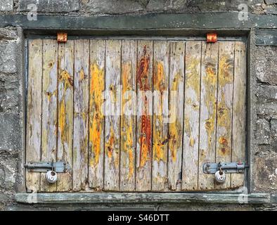 Verriegelte Holzluke mit abblätternder Farbe in Steinwand Stockfoto