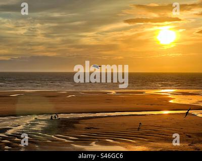 Sonnenuntergang am späten Abend über dem Nordstrand von Blackpool bei Ebbe mit Möwen und einer dreiköpfigen Familie Stockfoto