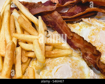 Nahaufnahme eines Frühstücks mit Spiegeleiern, knusprigem Speck und frittierten Pommes frites, 2023, New York City, USA Stockfoto