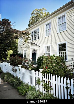Wunderschönes, altes, zweistöckiges Neuengland, Haus in Guilford, Connecticut, USA. Gelbes Haus mit weißem Streifenzaun. Charmanter kleiner Garten. Stockfoto