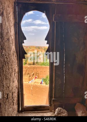 Ein Blick auf ein Berberdorf, Wüste und Palmen aus einem kleinen Fenster in einem Lehmhaus in Ait Benhaddou, Marokko Stockfoto