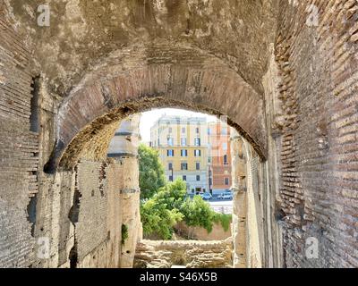 Blick von der Innenseite des römischen Kolosseums auf farbenfrohe Gebäude auf der Straße draußen. Stockfoto