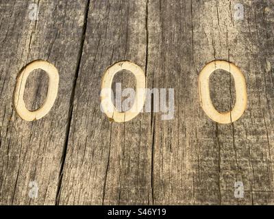 Drei weiße Zahlen 0 auf einem verwitterten Holzpfahl Stockfoto