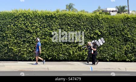 LOS ANGELES, CA, 30. Juni 2023: Mitglieder der IATSE Local 600 Camera union, mit Plakaten und Spaziergang an einer hohen Hecke in Hollywood während des Streiks von Schauspielern und Schriftstellern Stockfoto