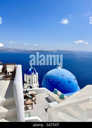 Die Kirche Saint Spyridon mit ihrer blauen Kuppel! Und Glockenturm unter Terrassen am steilen Hang der Küste von Oia, die hinunter in die Caldera von Santorin führt. Stockfoto