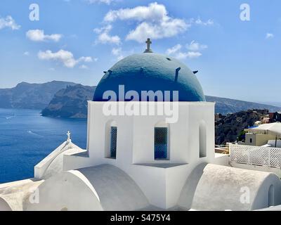 Die weiß getünchte, blaue Kuppelkirche St. Anastasi, vor dem blauen Himmel und dem blauen Wasser der Caldera unten in Santorin. Stockfoto