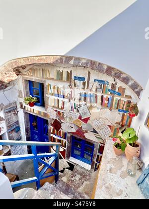 Das farbenfrohe Äußere eines Geschäfts in Santorin umfasst Bücher, die in einem Wandgemälde unter einem Backsteinbogen gemalt sind. Oia, Santorin. Stockfoto