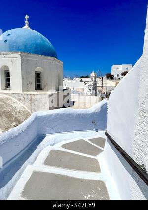 Wände in blassblau und weiß säumen einen gewundenen Treppenpfad, der hinunter zum Zentrum des Dorfes Megalochori führt, vorbei an der blauen Kuppelkirche Zoodochos Pigi. Santorin Stockfoto