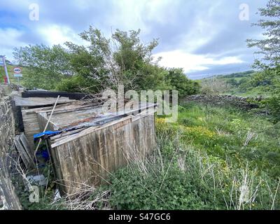 Alte Hütte, eingebettet in eine Ecke eines Feldes, mit Blumen, Gras und Bäumen, vor einem blauen Himmel, im Shibden Valley, Halifax, Yorkshire, England Stockfoto