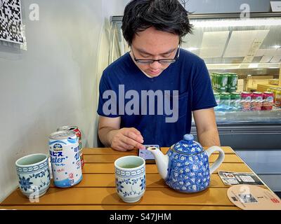 Junger asiatischer Mann in Brille mit QR/Quick Response Code und Handy, um Essen am Tisch in einem japanischen Restaurant zu bestellen. Wireless-Technologie. Stockfoto