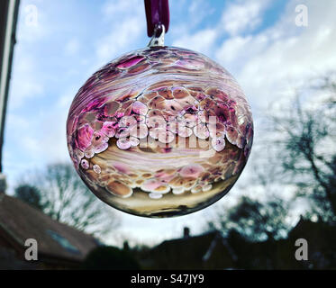 Rosafarbene, durchscheinende Weihnachtskugel hängt vom Fenster Stockfoto