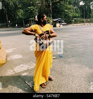 Eine Frau in einem gelben Sari, die die Straße in Mumbai überquert Stockfoto