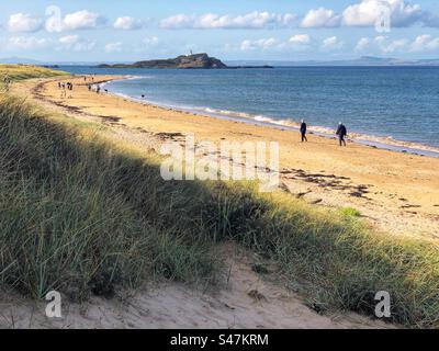 Leute, die am Yellowcraig Beach laufen, mit Blick auf den Leuchtturm Fidra, East Lothian Scotland Stockfoto