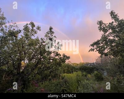 Atemberaubende Landschaft bei Sonnenuntergang mit Regenbogen in farbenfrohem Himmel aus rosa blauem Orange am ruhigen Sommerabend Stockfoto