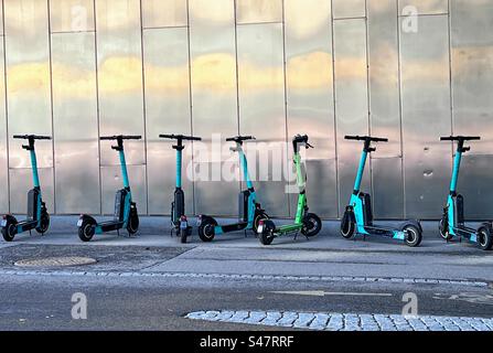 E-Scooter von Tier City parkten in einer Reihe auf dem Straßengang neben der glänzenden Metallbauwand Stockfoto