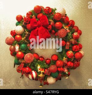 Schöner und extravaganter Weihnachtstürkranz mit roten Schleifen und Kugeln in einem quadratischen Rahmen und goldenen Hintergrund Stockfoto