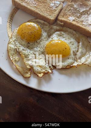 2 sonnige Eier auf weißem Teller mit gebuttertem Toast. Enthält Druckbereich. Stockfoto