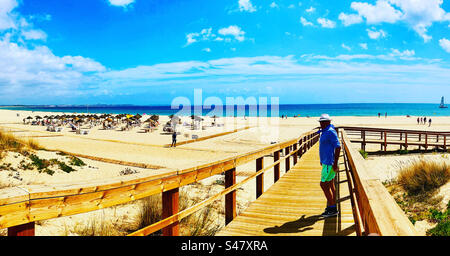 Mann, der auf einer Holzpromenade mit dem Strand von Meia Praia im Hintergrund in Lagos Portugal steht Stockfoto