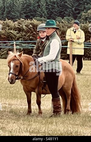 Kleinkind reitet Miniatur Shetland-Pony mit Mutter in einer traditionellen englischen Landshow Stockfoto