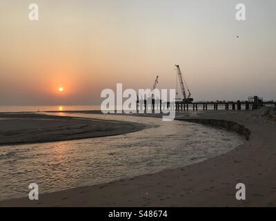 Kräne und schwere Bauarbeiten am Strand gegen die untergehende Sonne Stockfoto