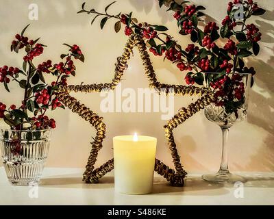 Beleuchtete Kerze vor dekorativem Weihnachtsrattanstern mit roten Cotoneaster-Beerenzweigen in Kristallgläsern mit Beleuchtung. Weihnachten. Feiern. Dekoration. Stillleben. Stockfoto