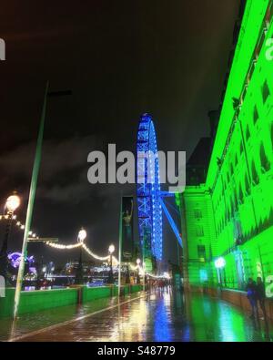 Ein Blick von der Westminster Bridge auf das London Millennium Wheel aka London Eye einschließlich County Hall und historischen Lichtern, die bei Nacht mit Reflexionen im Regen beleuchtet werden Stockfoto