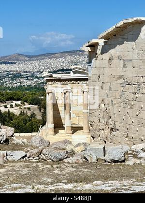 Tempel der Athena Nike, Göttin des Sieges, inmitten der beeindruckenden Ruinen auf dem Akropolis-Hügel mit der Stadt Athen und den Bergen im Hintergrund. Stockfoto