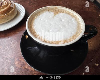 Cappuccino und schwedisches Zimtbrötchen auf rustikalem Restauranttisch für Fika (schwedische Kaffeepause) in Göteborg, Schweden. Stockfoto