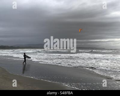 Cabedelo, Portugal - 11. November 2023: Ein Surfer, der als anderer Surfer mit einem orangen Drachen ins Wasser des Atlantischen Ozeans fährt Stockfoto