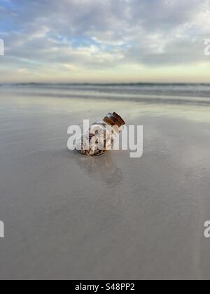 Kleine Flasche mit winzigen Muscheln auf Strandsand Stockfoto