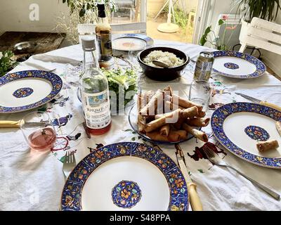 Aufnahme eines voll eingestellten Mittagstisch mit blauen, komplizierten Tellern, französischem Wein, weißem Reis, Frühlingsbrötchen Stockfoto