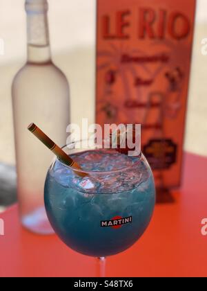 Ein blauer Lagunencocktail in einem Martini-Glas vor einer Flasche Wasser und ein Menü für ein französisches Restaurant namens Le Rio in Palavas-les-Flots, Occitanie, Frankreich Stockfoto