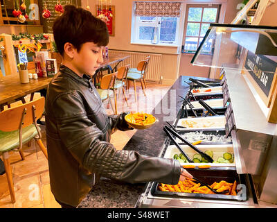 Ein Junge von hilft sich selbst zu einem Selbstbedienungsbuffet Salat in einem Harvester Restaurant. Stockfoto