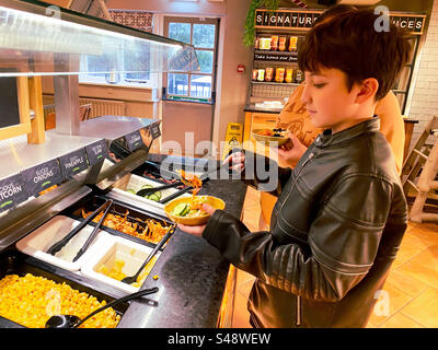 Ein Junge von hilft sich selbst zu einem Selbstbedienungsbuffet Salat in einem Harvester Restaurant. Stockfoto