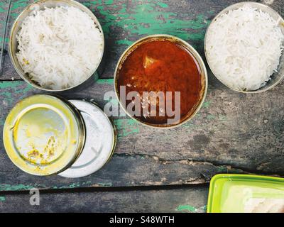 Indisches scharfes Hühnercurry und Reis in Lunchboxen auf einem Picknicktisch serviert Stockfoto
