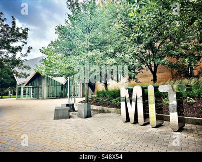 Cambridge, Massachusetts, USA: Massachusetts Institute of Technology - The Stata Center. Modernes, glänzendes Schild für mit auf dem Bürgersteig. Gebäude und Bäume als Teil der Universitätscampusszene. Stockfoto