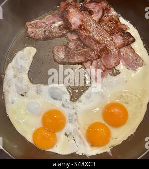 Speck und zwei doppelte Eier, die in einer Pfanne für ein Wochenendfrühstück gebraten werden Stockfoto