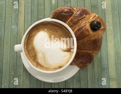 Frühstück mit Cappuccino und Kirschcroissant an der Bar Stockfoto