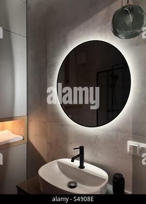 Modernes Badezimmer in schwachem Licht mit großem runden Spiegel mit Hintergrundbeleuchtung Stockfoto