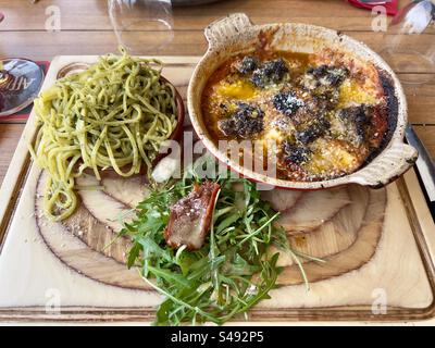 Schuss einer hölzernen Restaurantplatte mit einem Teller Pesto Spaghetti, Fleischbällchen in Tomatensauce mit Parmesan und grünem Salat mit Speck. Stockfoto