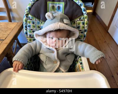 Das kleine Mädchen hat sich zusammengebündelt und wartet und sitzt in einem Hochstuhl. Stockfoto