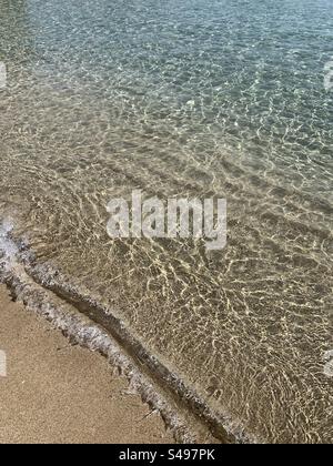 Klares Meer, das entlang der Küste auf den Sandstrand ragt Stockfoto