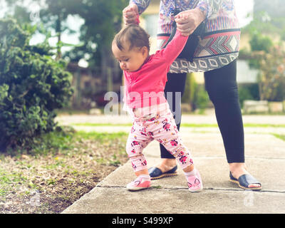 Die ersten Schritte Ihres Babys im Freien. Baby geht, das von einem Erwachsenen unterstützt wird Stockfoto