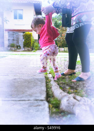Die ersten Schritte Ihres Babys im Freien. Das Baby läuft mit Aufregung und wird von einem Erwachsenen unterstützt Stockfoto